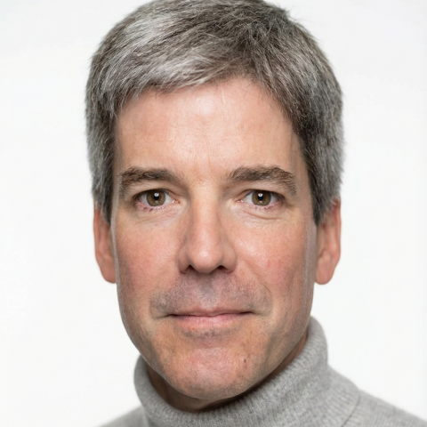 Headshot portrait of an individual photographed from the shoulders up against a plain light gray background, wearing a light gray turtleneck sweater. The individual faces forward with short, neatly styled hair and evenly lit features, centered in the frame. The image has a clean, studio-style composition with soft, neutral lighting.